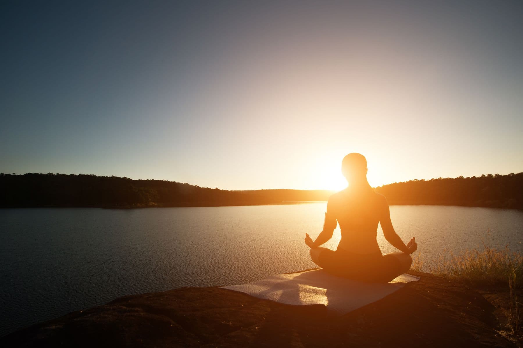 Silhouette meditating beside a lake at sunset