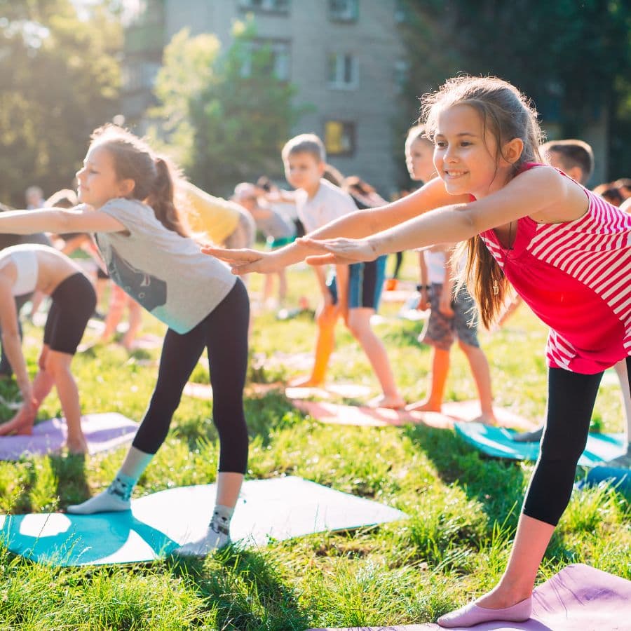 Children doing a balancing yoga pose together on grass